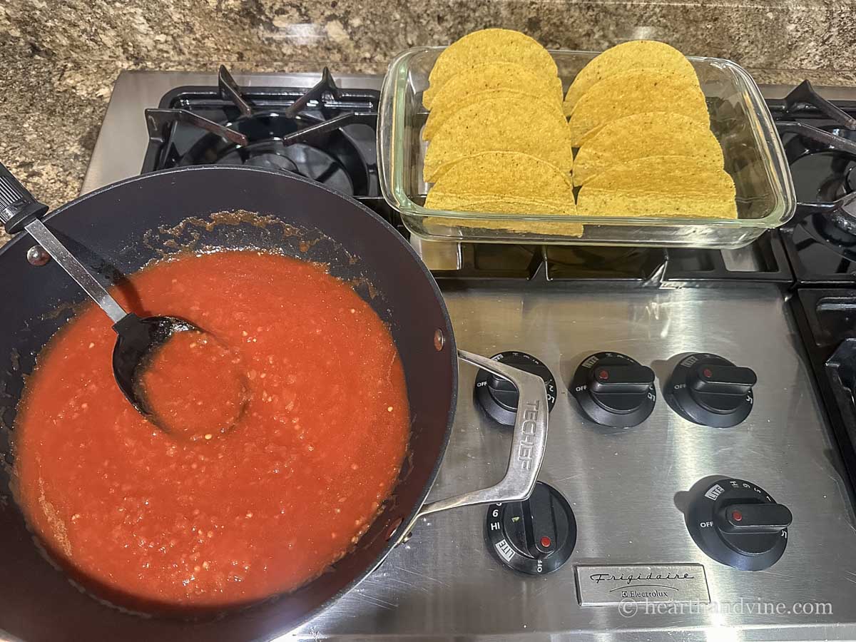 Large skillet on the stove with salsa and spices next to a baking pan with hard shell tacos.