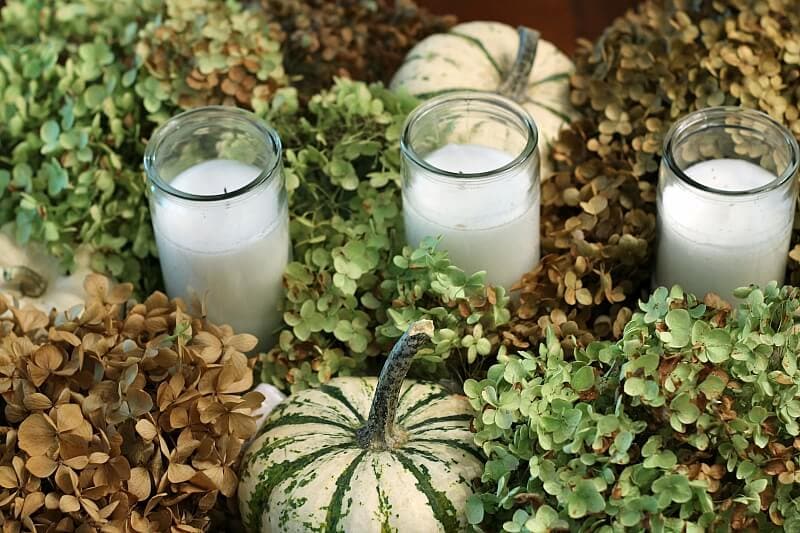 Fall centerpiece from above shows candles nestled into dried hydrangea and green and white pumpkins
